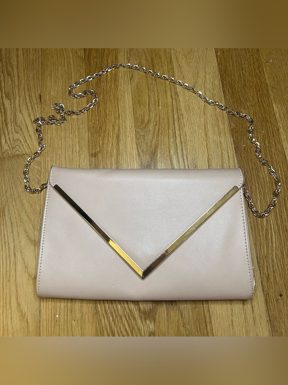 Pink crossbody bag with gold chain strap and gold V-shaped trim